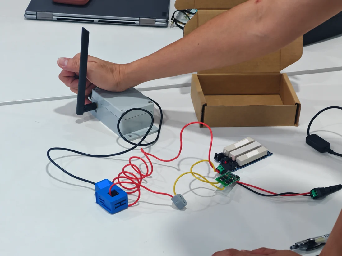 Bench demonstration of a clamp current sensor, test loads and wireless monitoring hub; labels redacted
