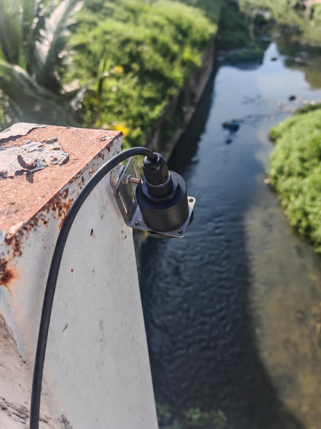 Non-contact radar sensor and bracket above a water channel; equipment markings redacted